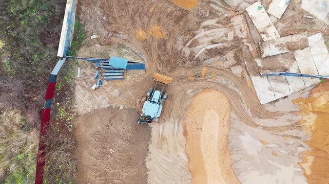Aerial view of heavy machinery at active construction site. Workers move materials, coordinate tasks under open sky. Earth is reshaped, concrete blocks stand in development phase