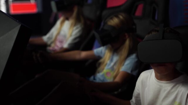 Young children wear VR headsets, seated in dim lighting. They focus intently on virtual worlds, hands resting on controls. Eyes close, heads tilted, showing total immersion