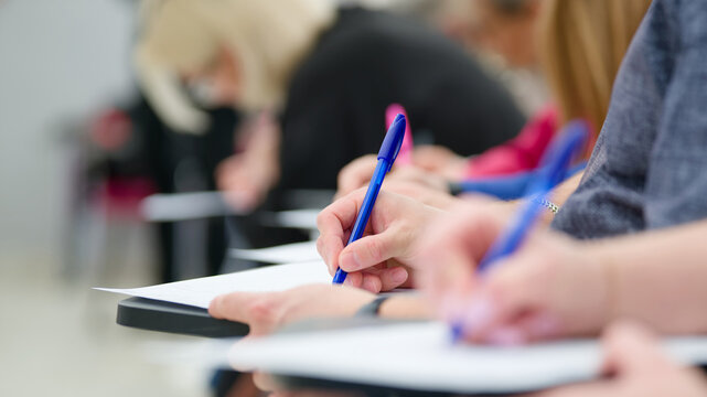 Selective focus on hands filling out a document or taking notes in a classroom. Group of young adults studying, learning and taking an academic test in a seminar. Photo