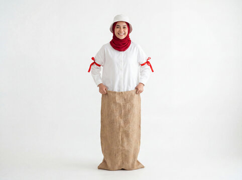 Cheerful Muslim Woman in Red Hijab White Bucket Hat and White Shirt with Red Ribbon Standing in Burlap Sack Ready for Sack Race Traditional Game Lomba Balap Karung Full Body on White Background