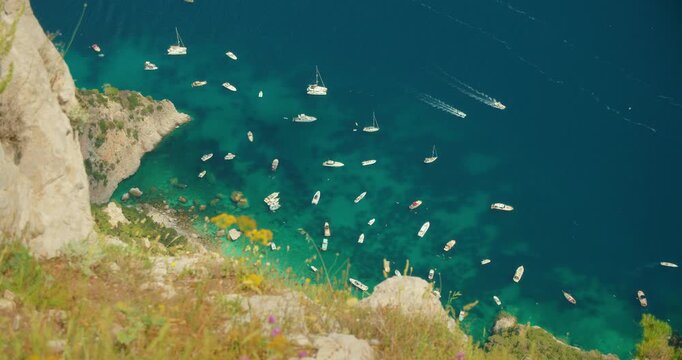 High view of turquoise shallows filled with anchored small boats on rocky coast of Capri Island Italy