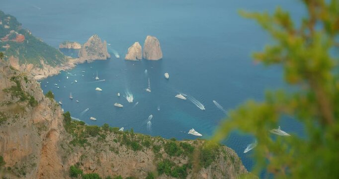 Boats travel across the blue sea near the Faraglioni cliffs seen from a high viewpoint in Capri Italy