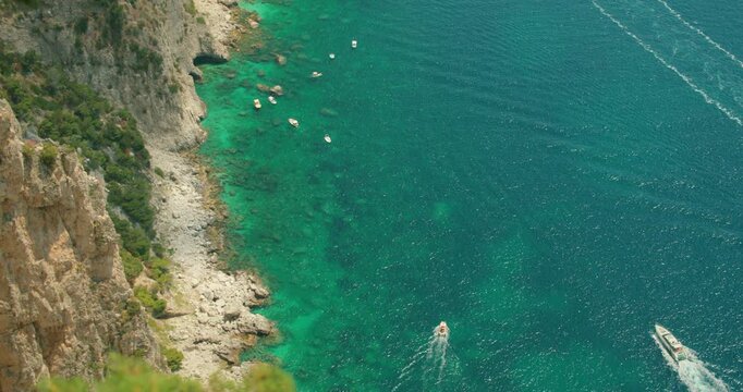A rocky Capri Italy coastline with turquoise sea and scattered pleasure boats and yachts near Faraglioni rock formations