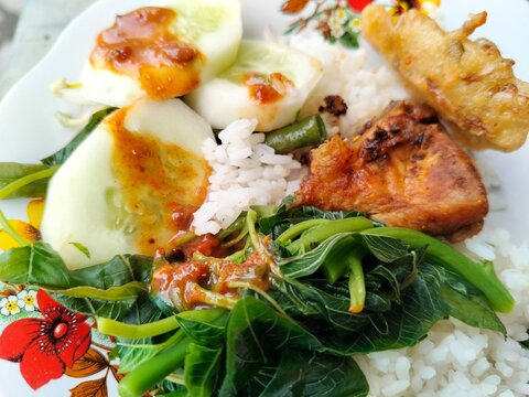 Traditional Indonesian food featuring white rice, crispy fried free-range chicken, pecel vegetable salad with peanut sauce, and savory bakwan fritters.