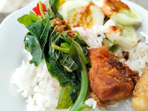 Traditional Indonesian food featuring white rice, crispy fried free-range chicken, pecel vegetable salad with peanut sauce, and savory bakwan fritters.