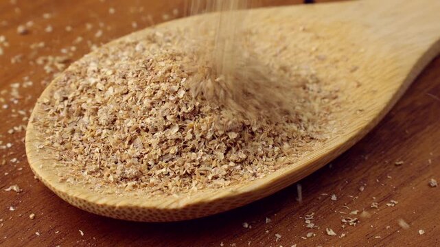 Organic Wheat Bran flakes falling down into the wooden spoon close up