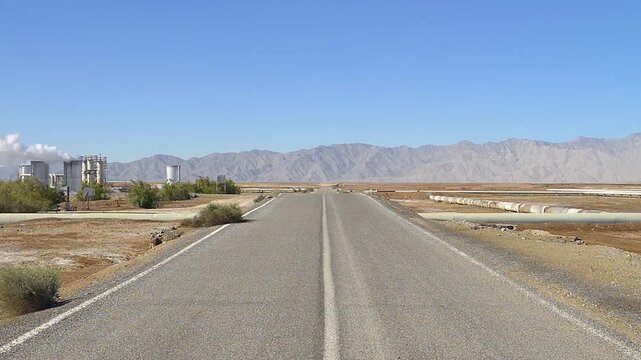 Road crossing a geothermal field for the production of electricity in Mexico, with steam drying wells on the left and mountains in the background, Mexican desert landscape
