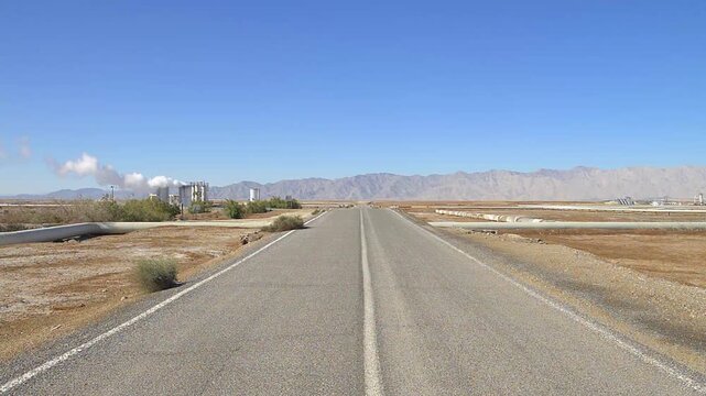 Road crossing a geothermal field for the production of electricity in Mexico, with steam drying wells on the left and mountains in the background, Mexican desert landscape
