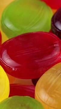 Glossy fruit-flavored hard candies in red, yellow, and green colors circle rotation close up, vertical video