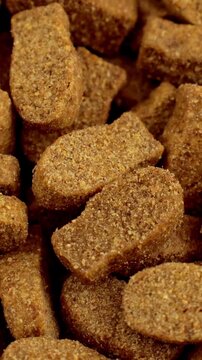 Brown kibble pieces of dry fish cat food circle rotation close up, vertical video format