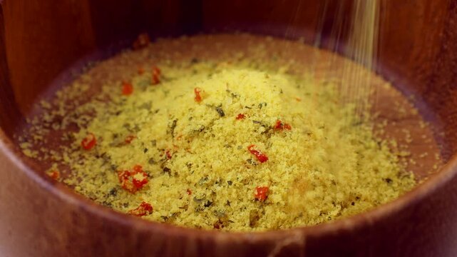 Yellow chicken stock powder seasoning falling down into the wooden bowl close up