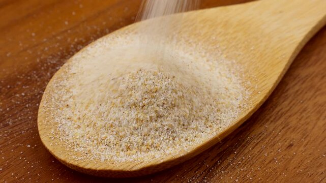 Dried granulated garlic falling down into the wooden spoon close up