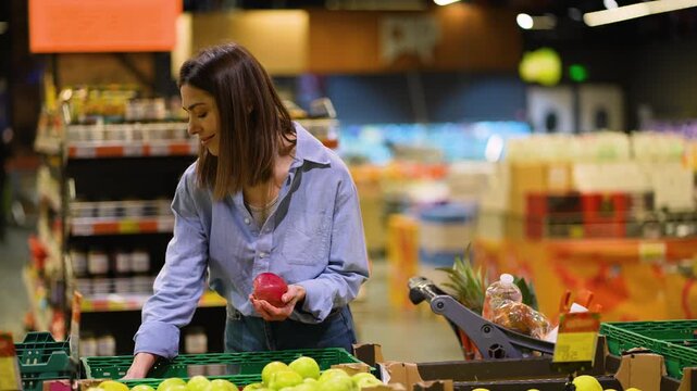 Young woman choosing fresh red apples in a supermarket