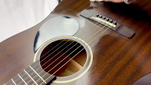 Close-up of cleaning the pickguard and bridge of an acoustic guitar with a white cloth.