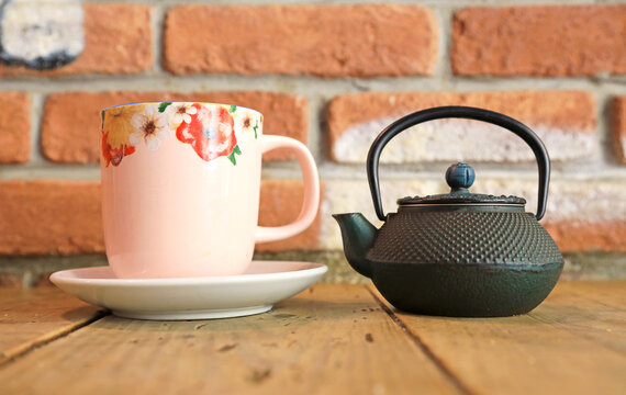 infusi&oacute;n de t&eacute; en una tetera de hierro fundido negra con una taza de t&eacute; color rosa sobre una mesa de madera y fondo pared de ladrillo 4M0A7322-as26