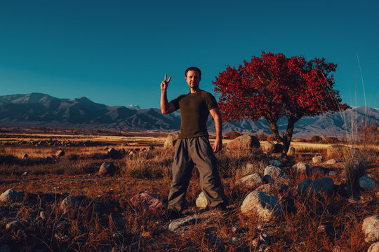 Man showing victory sign in scenic mountain field at sunset