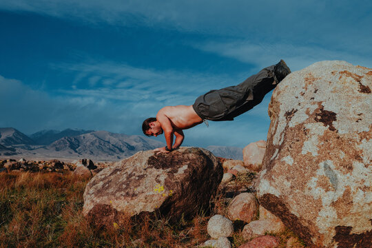 Shirtless man performing push up on rocks in mountains