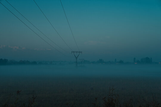 Foggy field with power lines and pylons in morning light