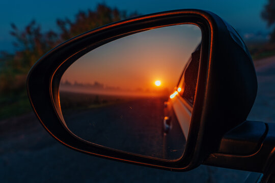 Car side mirror reflecting sunset road and landscape