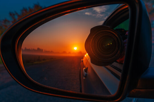 Camera lens reflected in car mirror at sunset, photography travel concept