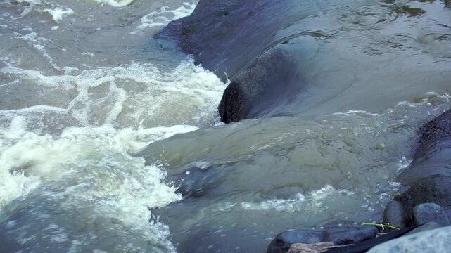 Fresh river water flowing rapidly over dark volcanic rocks at the cold lahar path of Mount Kelud, Indonesia, Southeast Asia during the afternoon.