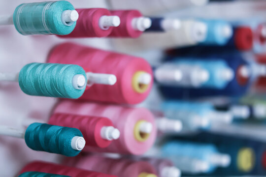 Side view of many colorful sewing thread spools on a vertical wall holder in a workshop