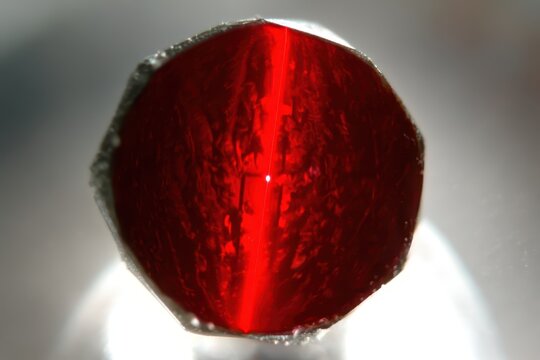 Close-up macro shot of a faceted red gemstone with a prominent chatoyancy effect and internal inclusions.