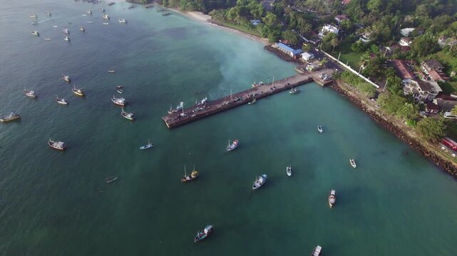 Arial pull out footage of a fishing boat dockyard in Sri Lanka. Shot on a sunrise and morning dew is visible and several boats are fishing in the blue water. 