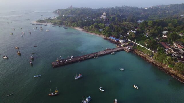 Arial pull out footage of a fishing boat dockyard in Sri Lanka. Shot on a sunrise and morning dew is visible and several boats are fishing in the blue water. 