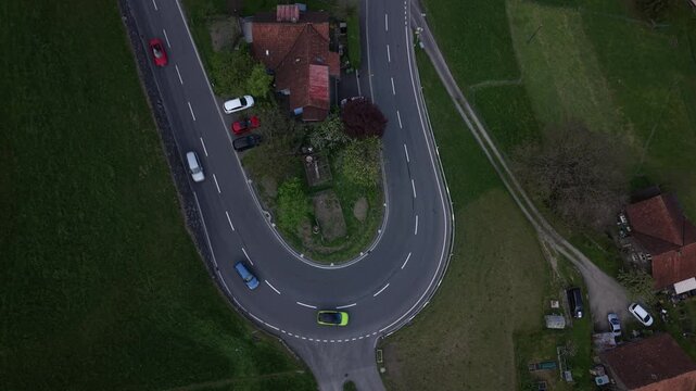 Top down aerial view of multiple cars and motorcycles navigating a tight mountain hairpin, showing traffic patterns and road structure.