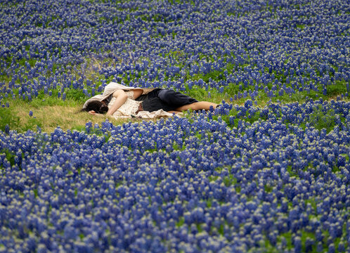 A couple relaxes in a field of bluebonnet flowers at the Muleshoe Bend Recreation Area near Marble Falls, Texas. People lying in grass on flowers.