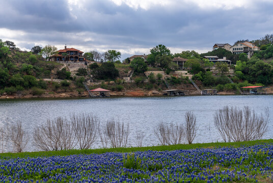 Picturesque view of lakefront homes across the water from bluebonnets at Turkey Bend Recreation Area in Marble Falls, Texas. Features Colorado River.