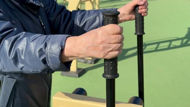 Woman exercising outdoors spring stadium wearing glasses beanie coat using leg exerciser on green rubber ground steady alternating.
