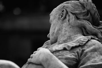 Fototapeta premium Black and white closeup of crying angel statue seen from behind, symbol of grief, loss and loneliness
