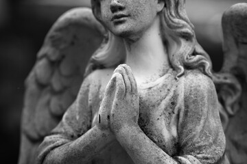 Fototapeta premium Black and white closeup of praying angel statue, hands together, symbol of faith, hope, peace and spirituality
