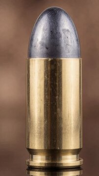 Close up of golden metal bullet on brown background, ammunition detail and texture concept, vertical video macro view.
