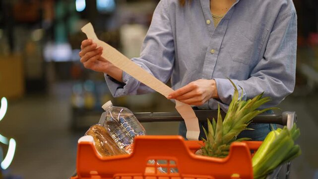 Woman checking long grocery receipt in supermarket