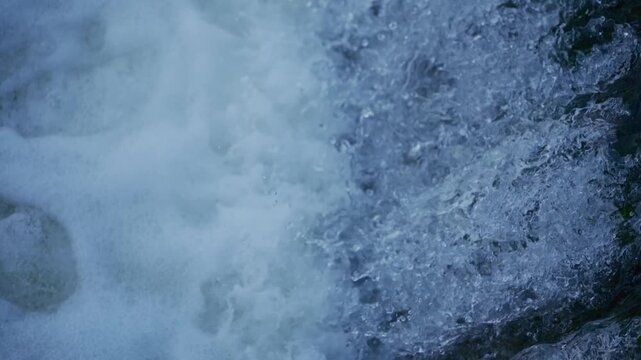 Water cascades over river barrier forming waterfall with foam bubbles and aerated flow captured in slow motion