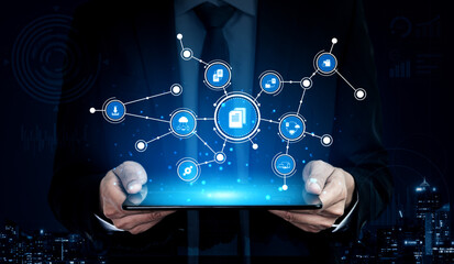 Obraz premium A businessman in a suit holds a tablet displaying digital network icons, showcasing concepts of data management, technology, and communication in a modern urban setting. Tessel