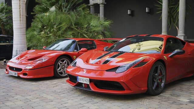 Maspalomas, Las Palmas, Canary Islands, Spain - April 13, 2024 - Two iconic red Ferrari sports cars, a F50 and a 458, parking on a paved ground in front of palm trees and a building