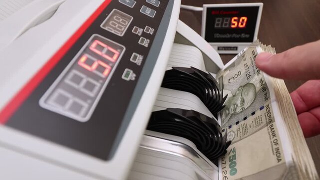 Closeup shot of banknote counting machine with Indian rupee (INR) money. Automatic currency counter equipment processing 500 rupees with Mahatma Gandhi portrait. Finance and banking industry in India.