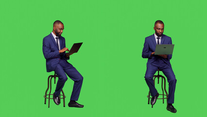 Corporate employee searching on online website, sitting on chair and using laptop in studio. Adult entrepreneur working with internet network page on wireless computer, full body greenscreen. © DC Studio