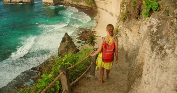 Hiker in dress walking down a steep seaside path to Diamond beach in Nusa Penida Bali