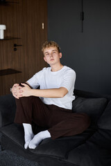 Fototapeta premium Young man with white skin relaxes on dark sofa in living room
