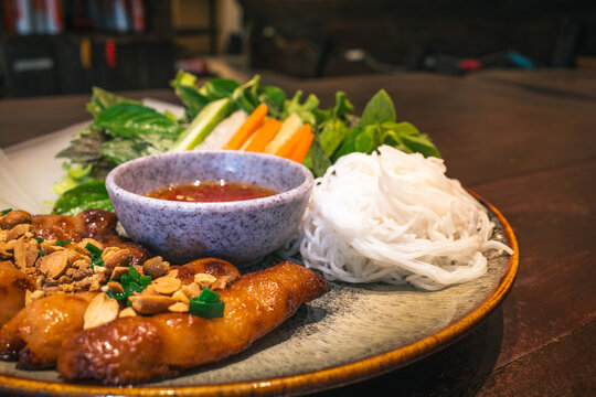 Close-up horizontal shot of Vietnamese Nem Nuong pork platter with rice noodles and fresh greens.