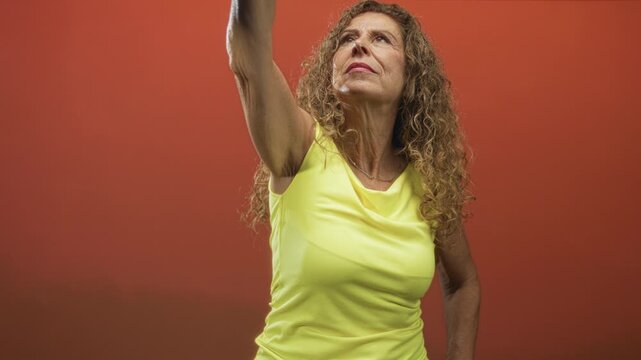 Middle age woman raises her arm and looks upward showing bare upper arm in a studio; determination resilience strength.