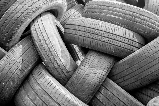 Black and white close-up of a pile of used car tires stacked chaotically. Abstract background with detailed tread pattern texture. Automotive, recycling and waste concept.
