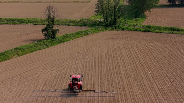 Tractor Cultivating a Field: An aerial view showcases a red tractor meticulously plowing a large, dry agricultural field, leaving behind neat rows and hinting at the upcoming planting season.