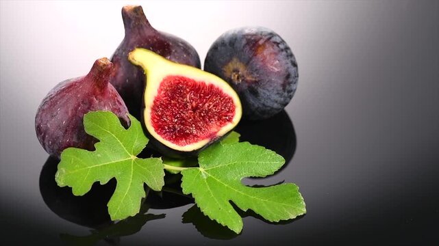 Fig fruit. Ripe sweet fresh figs fruits with leaves close up, on black background with water drops. Healthy sweet Mediterranean organic fruits. Vegan food. Slow mo
