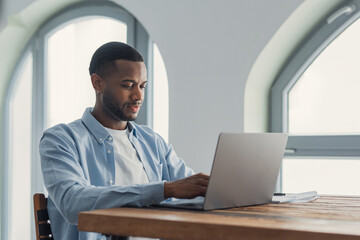 Naklejka na ściany i meble Young man working on laptop at home office by arched window, remote work and concentration
